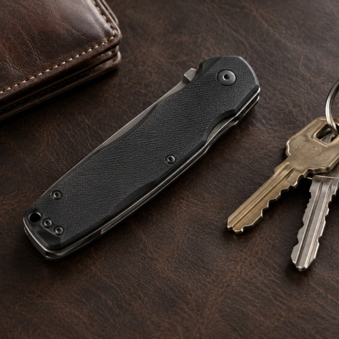 Closed folding knife next to keys and a wallet on a leather surface