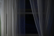 Sheer white curtains partially open with a dark background