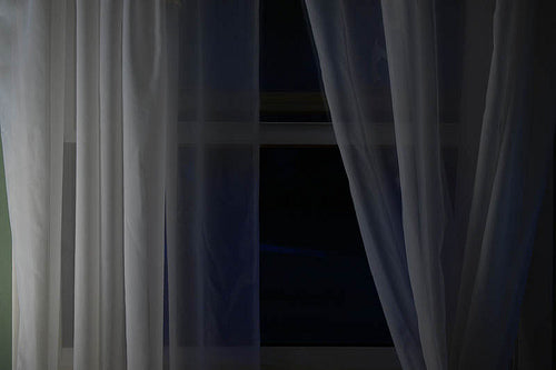 Sheer white curtains partially open with a dark background